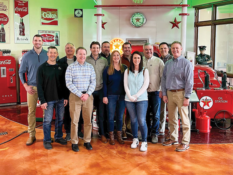Group of thirteen smiles in a retro gas-station museum with Coca-Cola and Texaco signs.